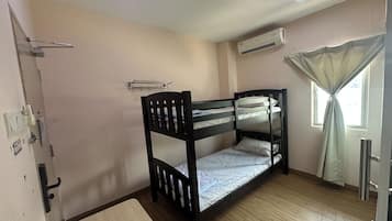 A bunk bed room with a wooden floor, a window with curtains, an air conditioning unit, and a door with a handle.