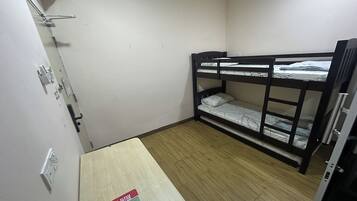 A small, sparsely furnished room with a bunk bed, a wooden table, and a wall-mounted air conditioner.