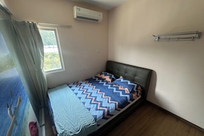 A single bed with a patterned bedspread, a window with curtains, an air conditioning unit, and a metal towel rack. - Abc Hostel By Zuzu (Seri Kembangan)
