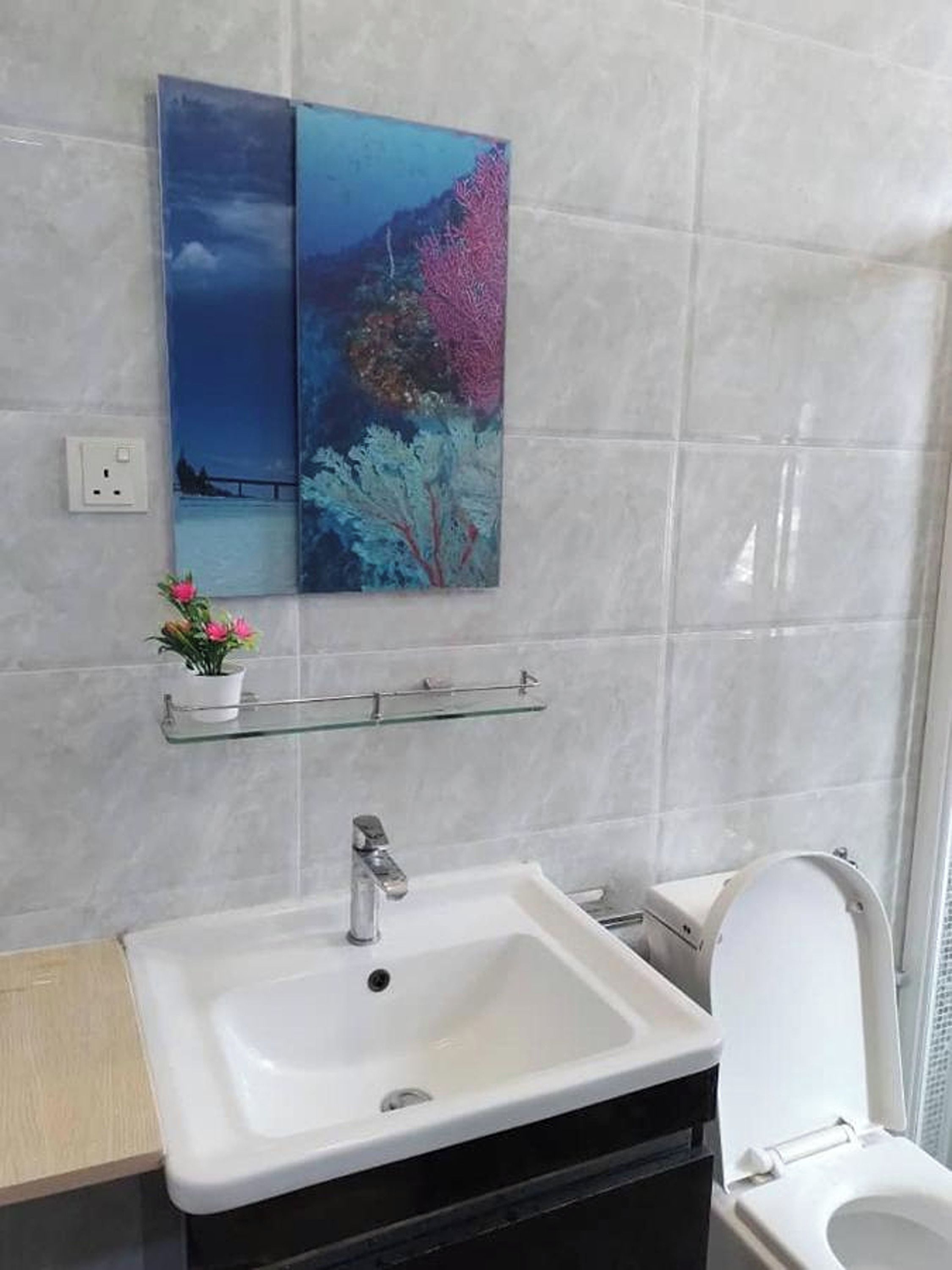 A bathroom with a white sink, a glass shelf with a potted plant, and a painting of a landscape on the wall.