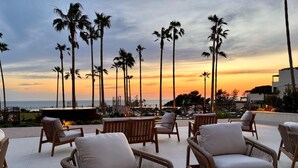 A terrace with wicker chairs and tables, overlooking a sunset and palm trees. - Punta Bermeja Premium Beach Hotel (El Puerto de Santa Maria)