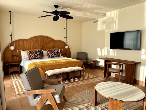 Une chambre d’hôtel avec un grand lit, un bureau, une chaise, une télévision et un ventilateur de plafond.