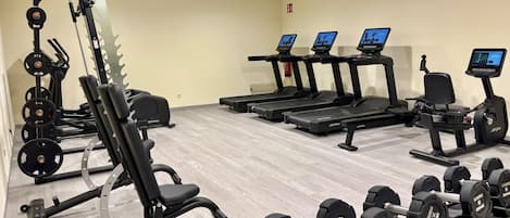 Un gimnasio con equipo de ejercicio variado, incluyendo cintas de correr, máquinas de pesas y mancuernas.