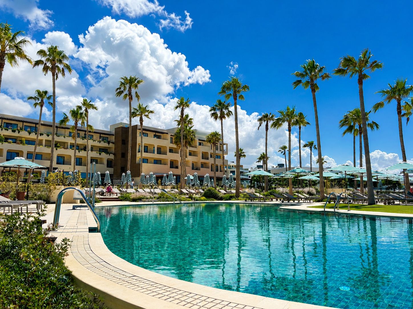 Ein Poolbereich eines Resorts mit Palmen, Liegestühlen und einem Gebäude mit mehreren Balkonen.