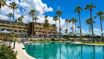 Ein Poolbereich eines Resorts mit Palmen, Liegestühlen und einem Gebäude mit mehreren Balkonen.