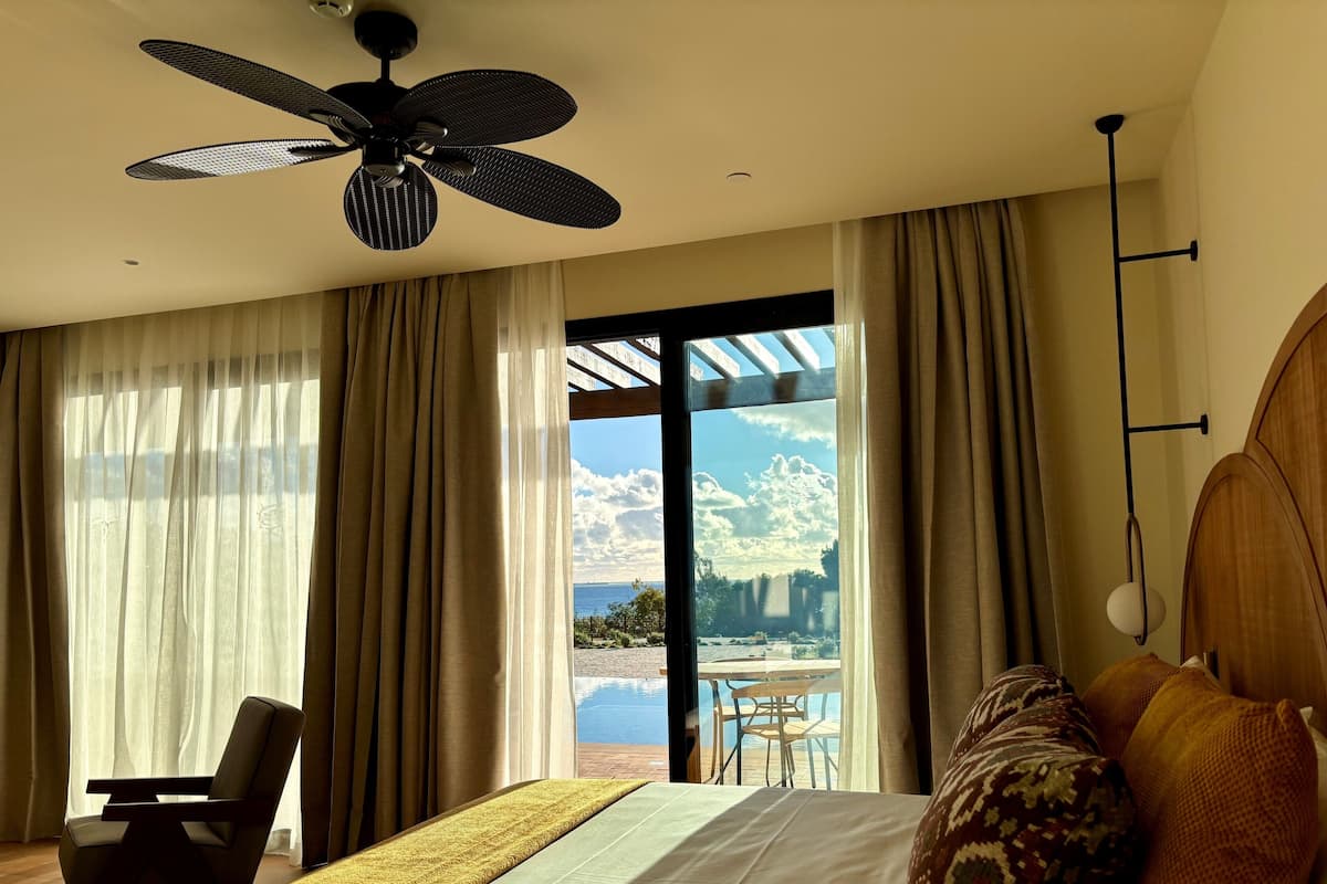 Ein Hotelzimmer mit Bett, Stuhl, Deckenventilator und Blick ins Freie.
