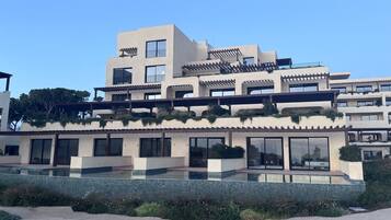 Un immeuble moderne à plusieurs étages, doté de balcons, de grandes fenêtres et d’un espace piscine.