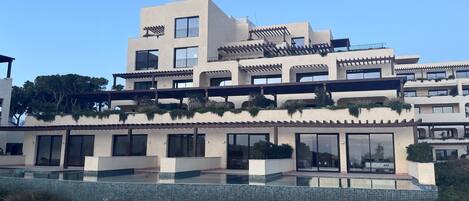 Un moderno edificio de varios pisos con balcones, ventanas amplias y una zona de piscina.