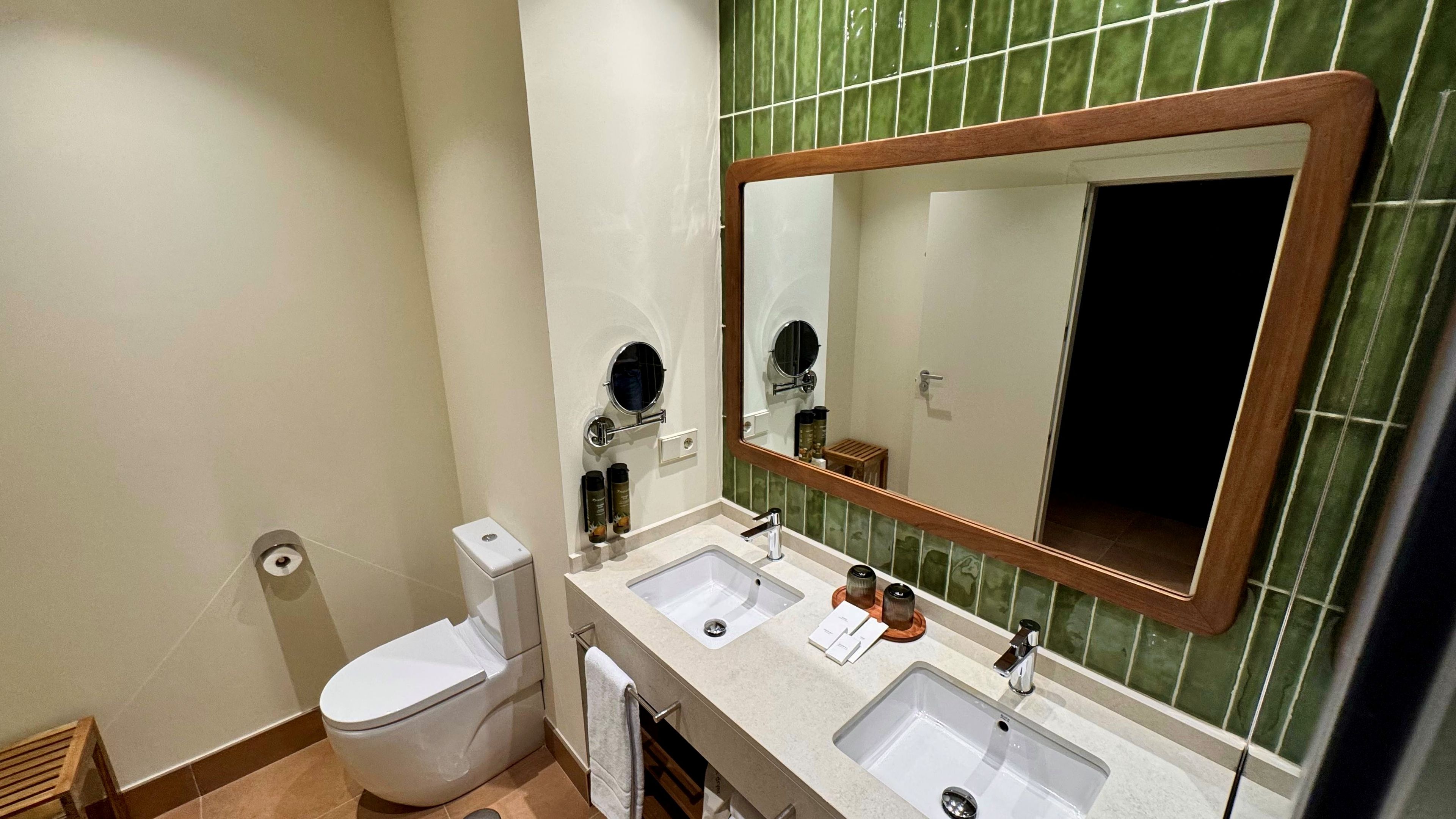 A bathroom with a toilet, two sinks, a mirror, and a towel rack.