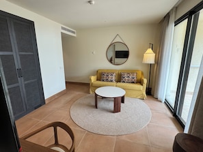 A living room with a sofa, a coffee table, a chair, a lamp, and a large window. - Punta Bermeja Premium Beach Hotel (El Puerto de Santa Maria)