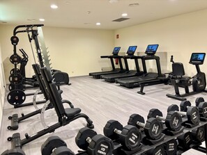 Une salle de sport équipée de divers appareils d’exercice, notamment des tapis de course, des appareils de musculation et des haltères.