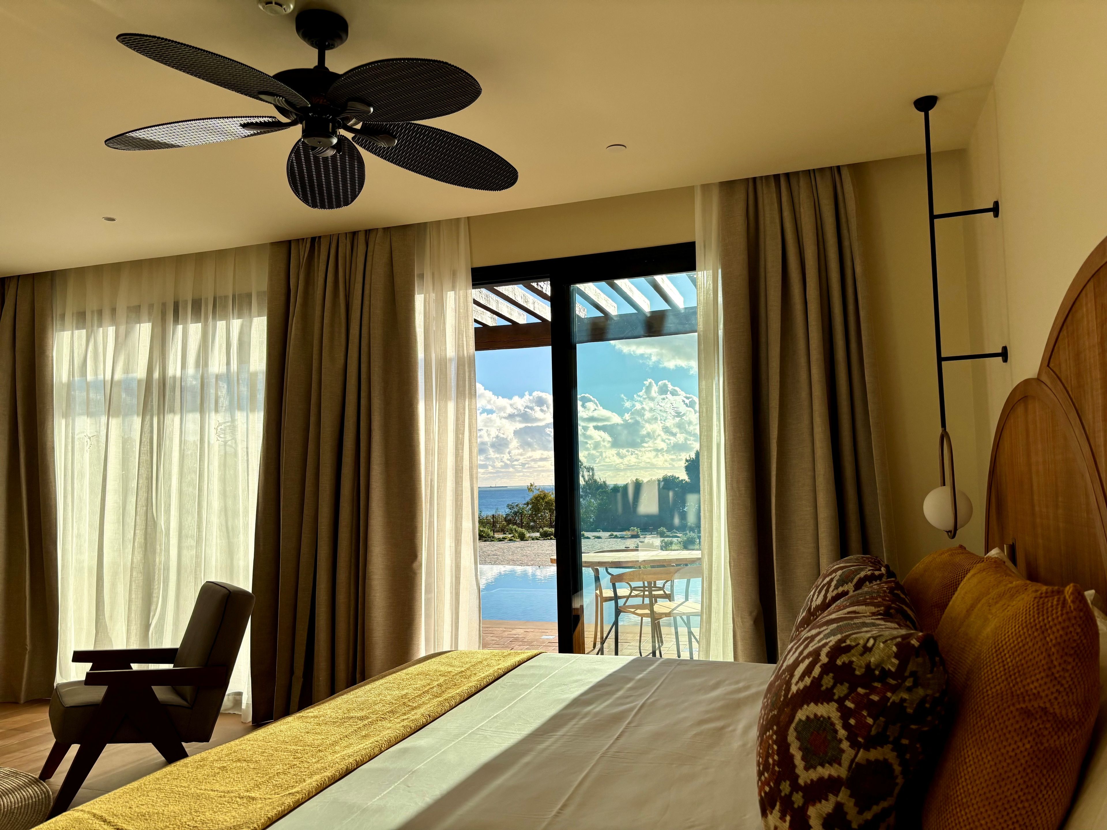 A hotel room with a bed, a chair, a ceiling fan, and a view of the outdoors.