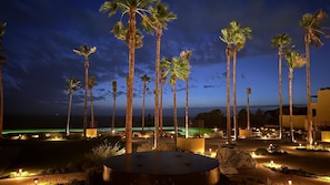 A nighttime view of a resort with palm trees, a pool, and a well-lit walkway. - Punta Bermeja Premium Beach Hotel (El Puerto de Santa Maria)