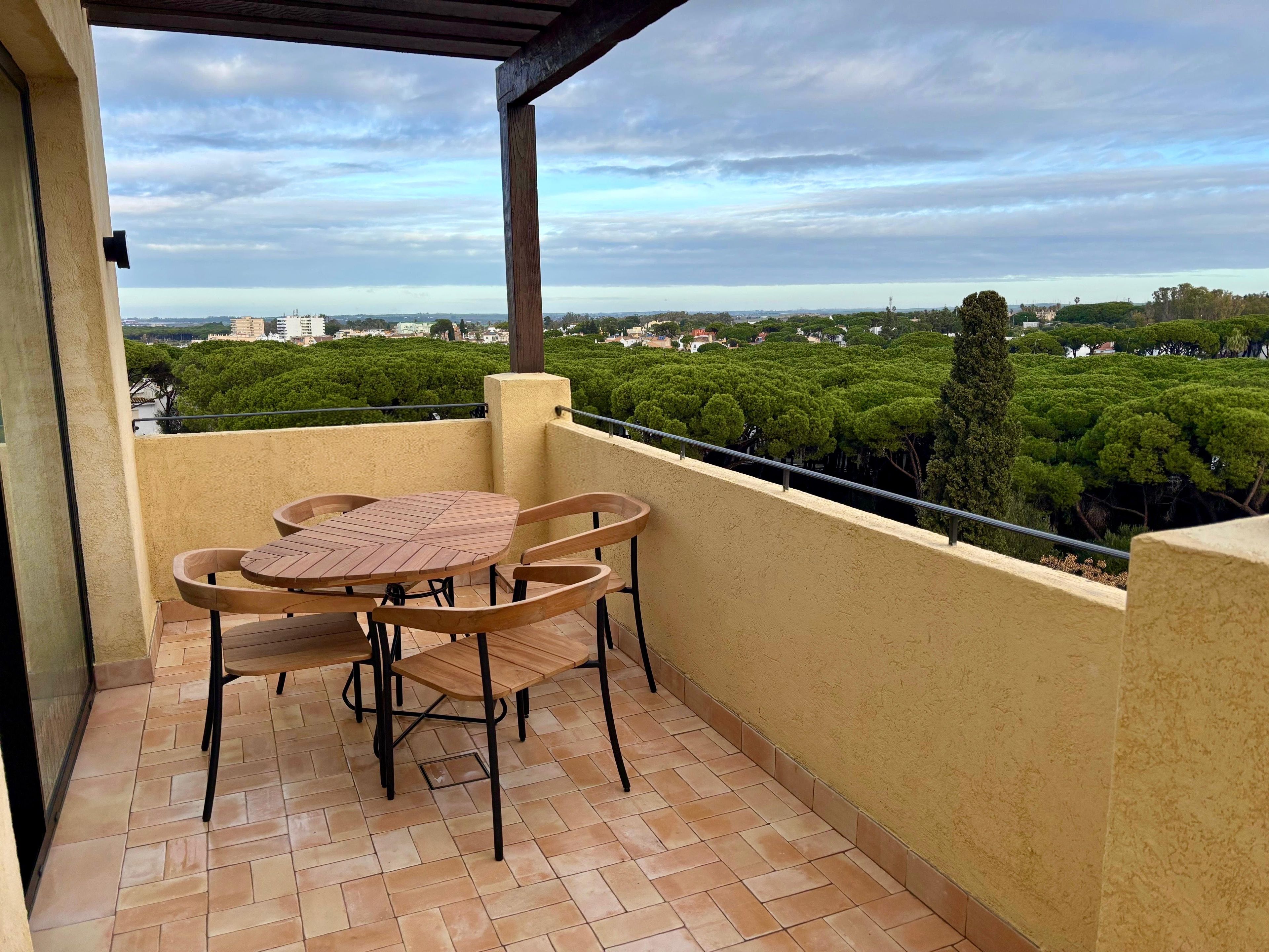 Ein Balkon mit Tisch und Stühlen, ein Fliesenboden sowie ein Blick auf eine grüne Landschaft und Gebäude.