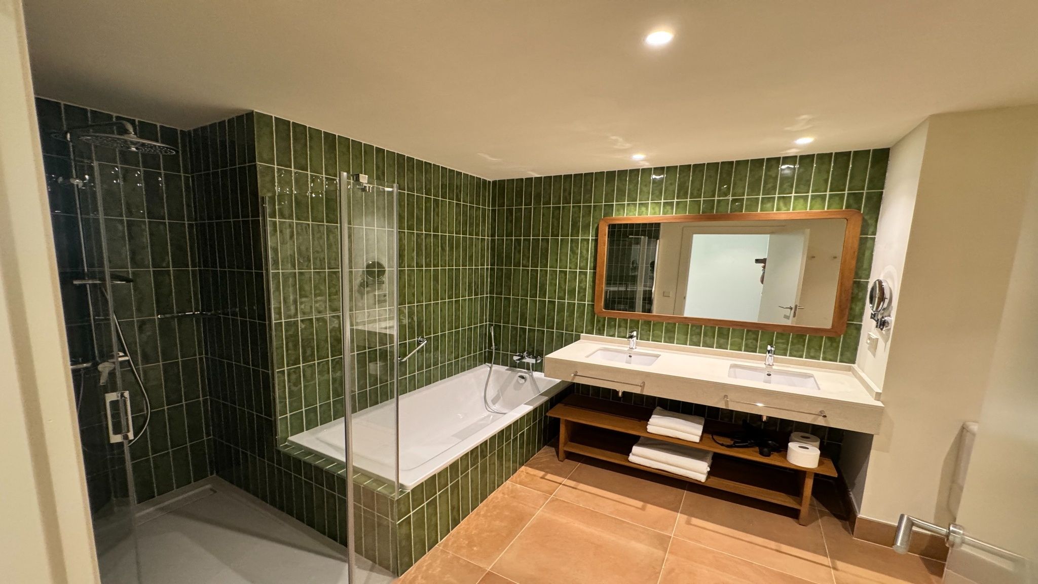 Un baño con ducha envuelta en vidrio, una bañera blanca y un lavamanos con dos lavabos.