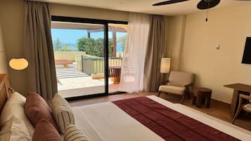 Habitación de hotel con una cama grande, una silla, una mesita y vistas a un balcón con mobiliario exterior.