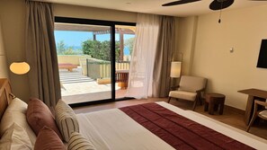 A hotel room with a large bed, a chair, a small table, and a view of a balcony with outdoor furniture. - Punta Bermeja Premium Beach Hotel (El Puerto de Santa Maria)