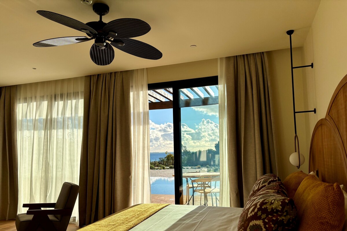 Camera d'albergo con un letto, una sedia, una ventola a soffitto e vista sull'esterno.