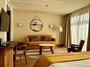 Une chambre d’hôtel avec un lit, un canapé, un bureau et une chaise. On y trouve également un ventilateur de plafond, une lampe et un téléviseur fixé au mur.