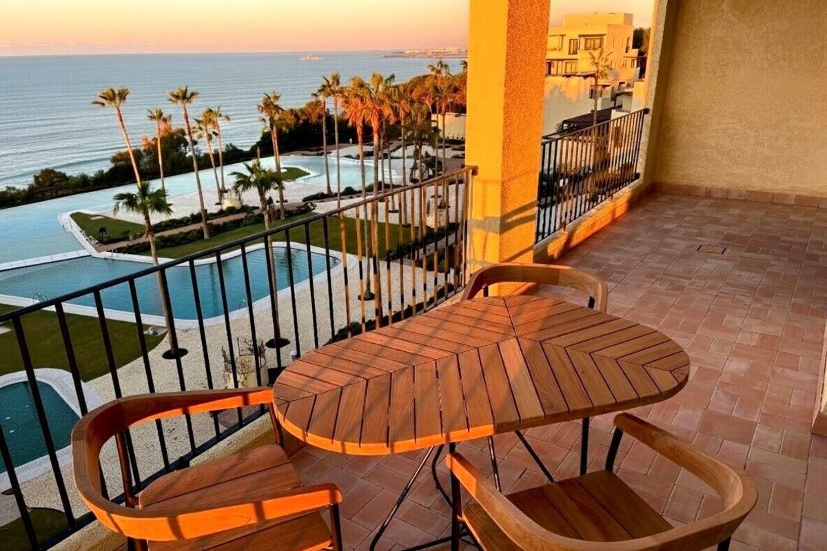 Ein Balkon mit Holztisch und -stühlen mit Blick auf einen Pool und Palmen.