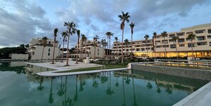 Un hotel con piscina, palmeras y un atardecer.