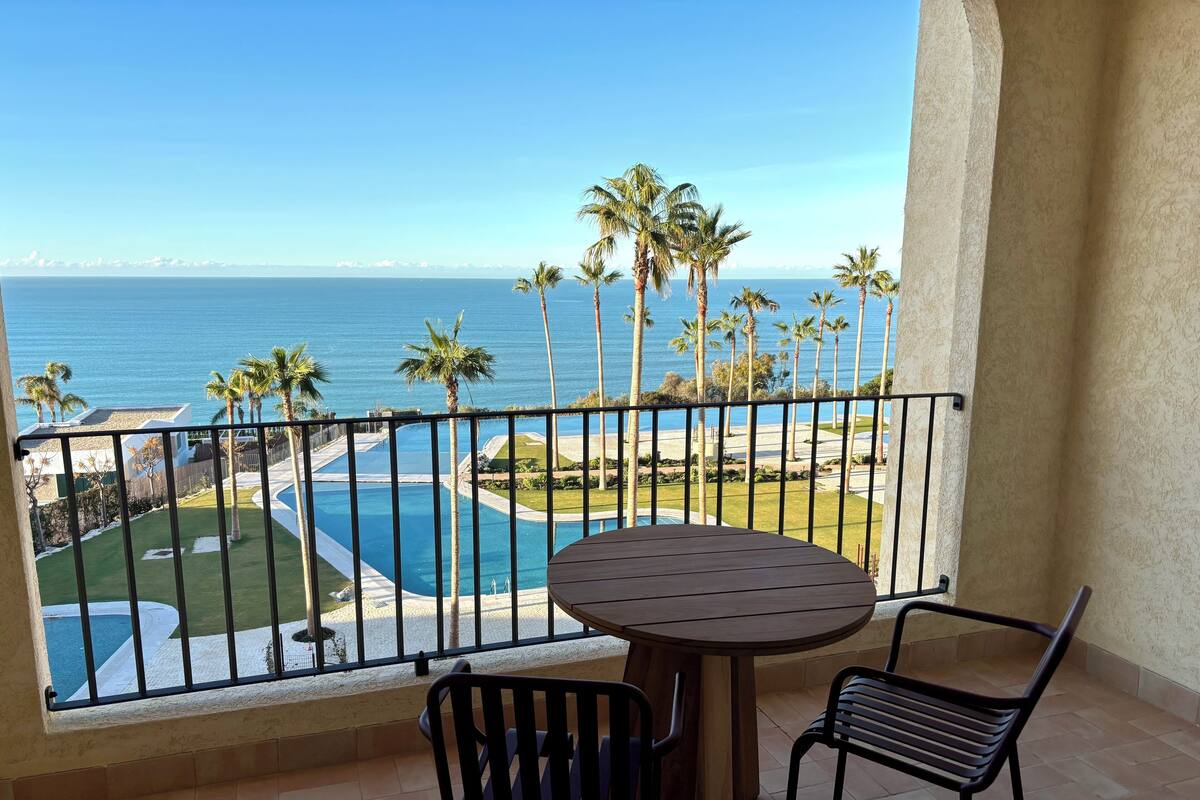 Ein Balkon mit Blick auf einen Swimmingpool und Palmen, einem runden Tisch und zwei Stühlen.
