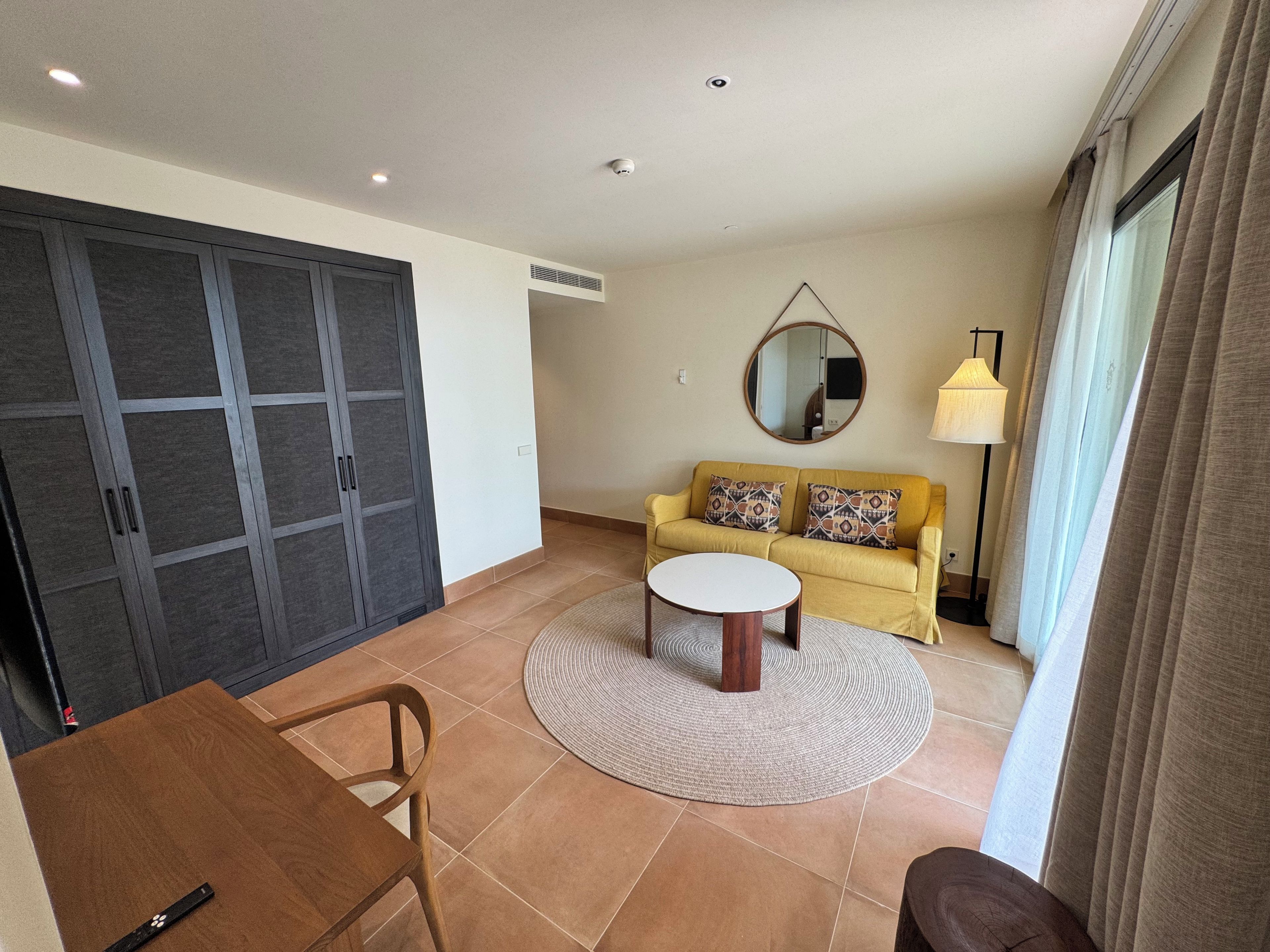 Een woonkamer met een bank, een rond bijzettafeltje, een eettafel met stoelen, en een kledingkast.