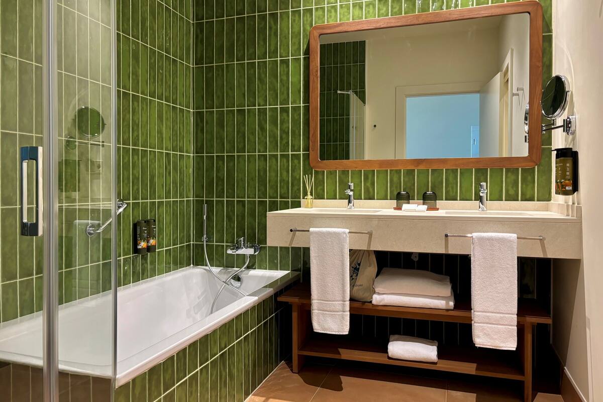 Ein Badezimmer mit einer gläsernen Duschkabine, einem Holzausleger und grünen Fliesenwänden.