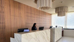 Una moderna recepción con encimeras de mármol, paneles de madera en las paredes y un amplio ventanal con luz natural.