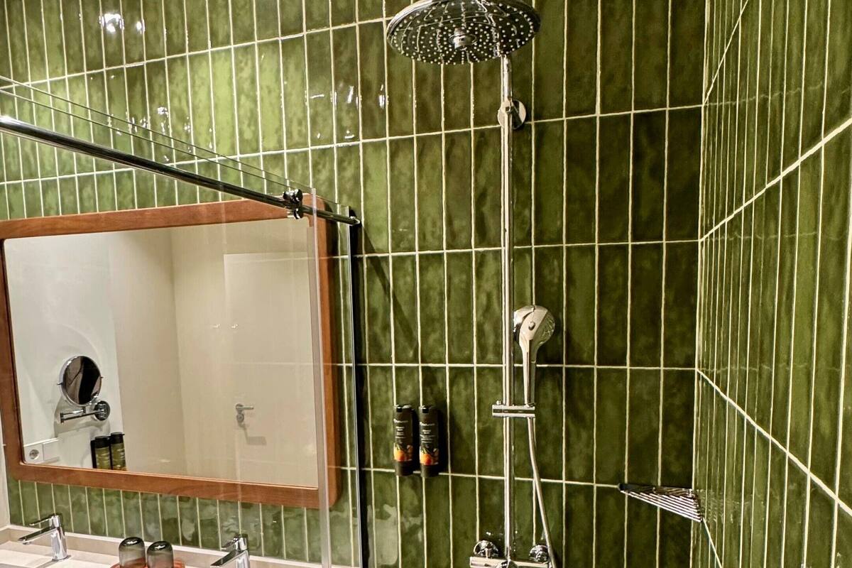 Ein Badezimmer mit grüner Fliesenwand, einer Dusche, einem Waschbecken mit Spiegel und einem Handtuchhalter.