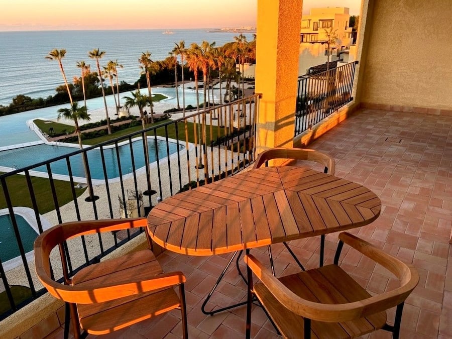 Un balcone con tavolo e sedie in legno, vista su una piscina e palme.