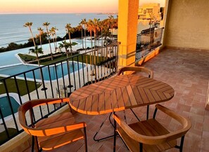 Ein Balkon mit Holztisch und -stühlen mit Blick auf einen Pool und Palmen.