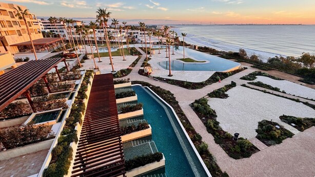 A resort with a swimming pool, palm trees, and a view of the ocean. - Punta Bermeja Premium Beach Hotel (El Puerto de Santa Maria)