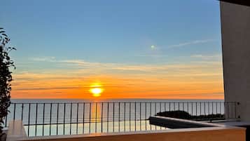 Un balcón con vistas a la puesta de sol sobre el mar, una barandilla y escaleras que bajan.