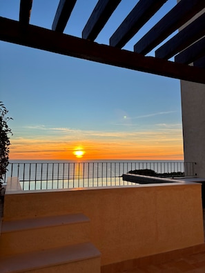 Un balcon offrant une vue sur le coucher de soleil sur la mer, une balustrade et des marches descendant vers le bas.