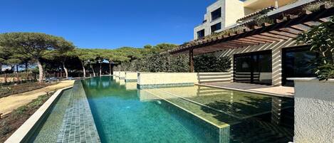 A modern pool area with clear water, surrounded by a landscaped garden and a contemporary building with large windows.