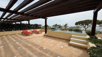 Ett takförsett utomhusområde med en pool, två röda solstolar och utsikt över havet.