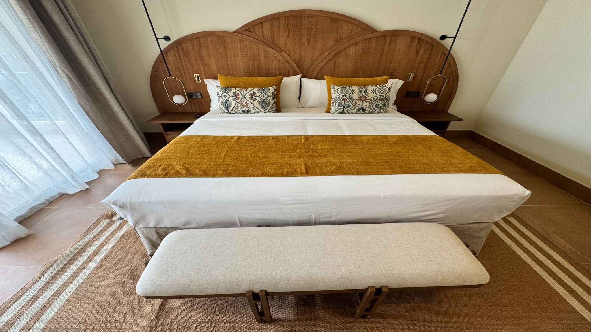 Un lit bien fait, avec une tête de lit en bois, un banc au pied du lit et un plaid à motifs.