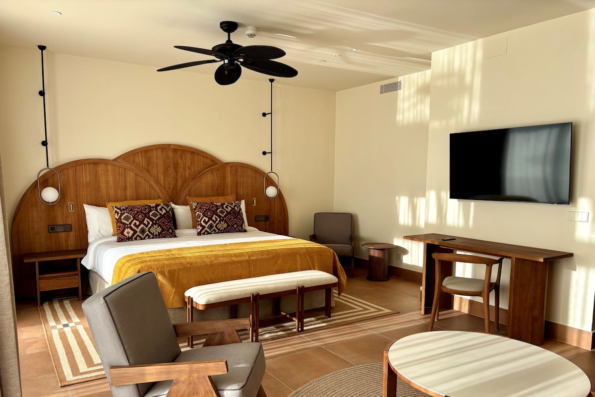 Ein Hotelzimmer mit einem großen Bett, einem Schreibtisch, einem Sessel, einem Fernseher und einem Deckenventilator.