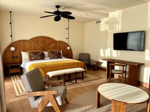 Habitación de hotel con una cama grande, un escritorio, una silla, un televisor y un ventilador de techo.