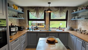 Una cocina moderna con armarios grises, una isla de acero inoxidable y vistas a un jardín a través de amplios ventanales.