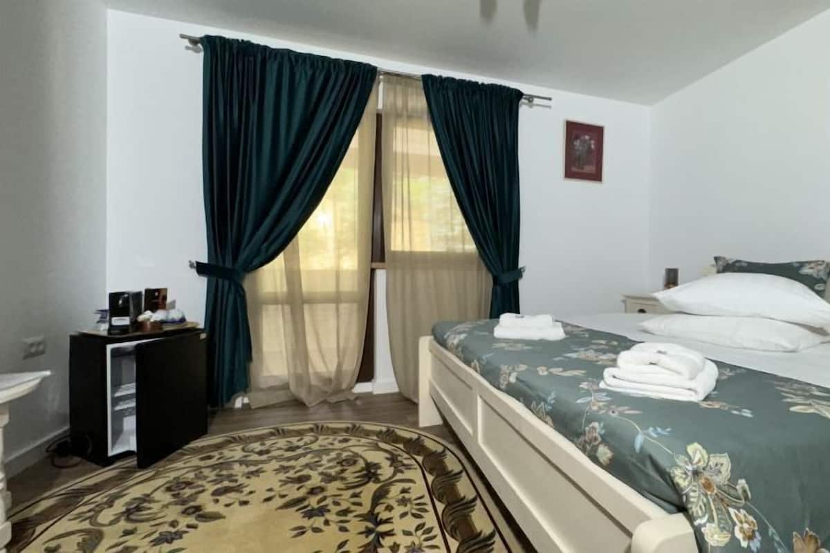 A hotel room with a bed, a desk, a chair, a small table, and a window with curtains.