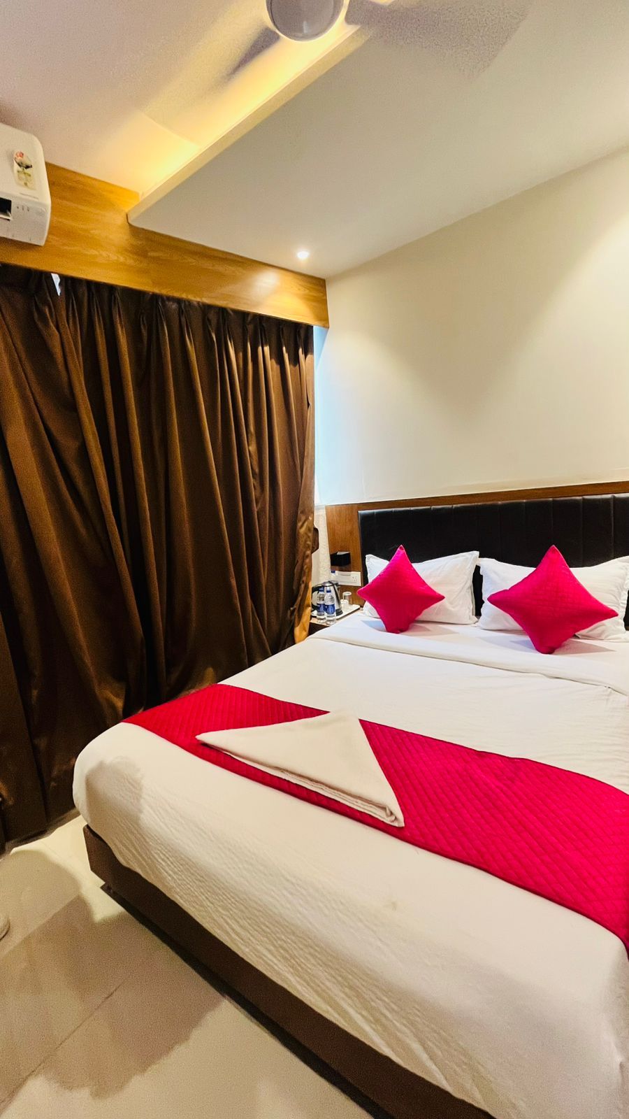A hotel room with a large bed, brown curtains, a wooden headboard, and a ceiling fan.