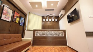 A modern reception area with a wooden reception desk, a brown sofa, and a wall-mounted TV. - Hotel The Azure (Mumbai)