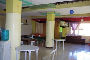 A dining area with tables and chairs, a water dispenser, and a television on the wall.