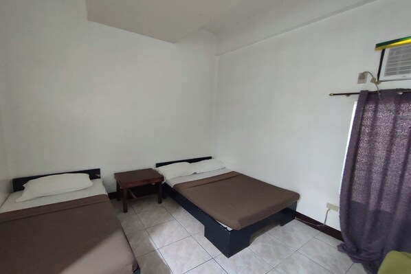 Una habitación con dos camas individuales, una mesita pequeña y una cortina.