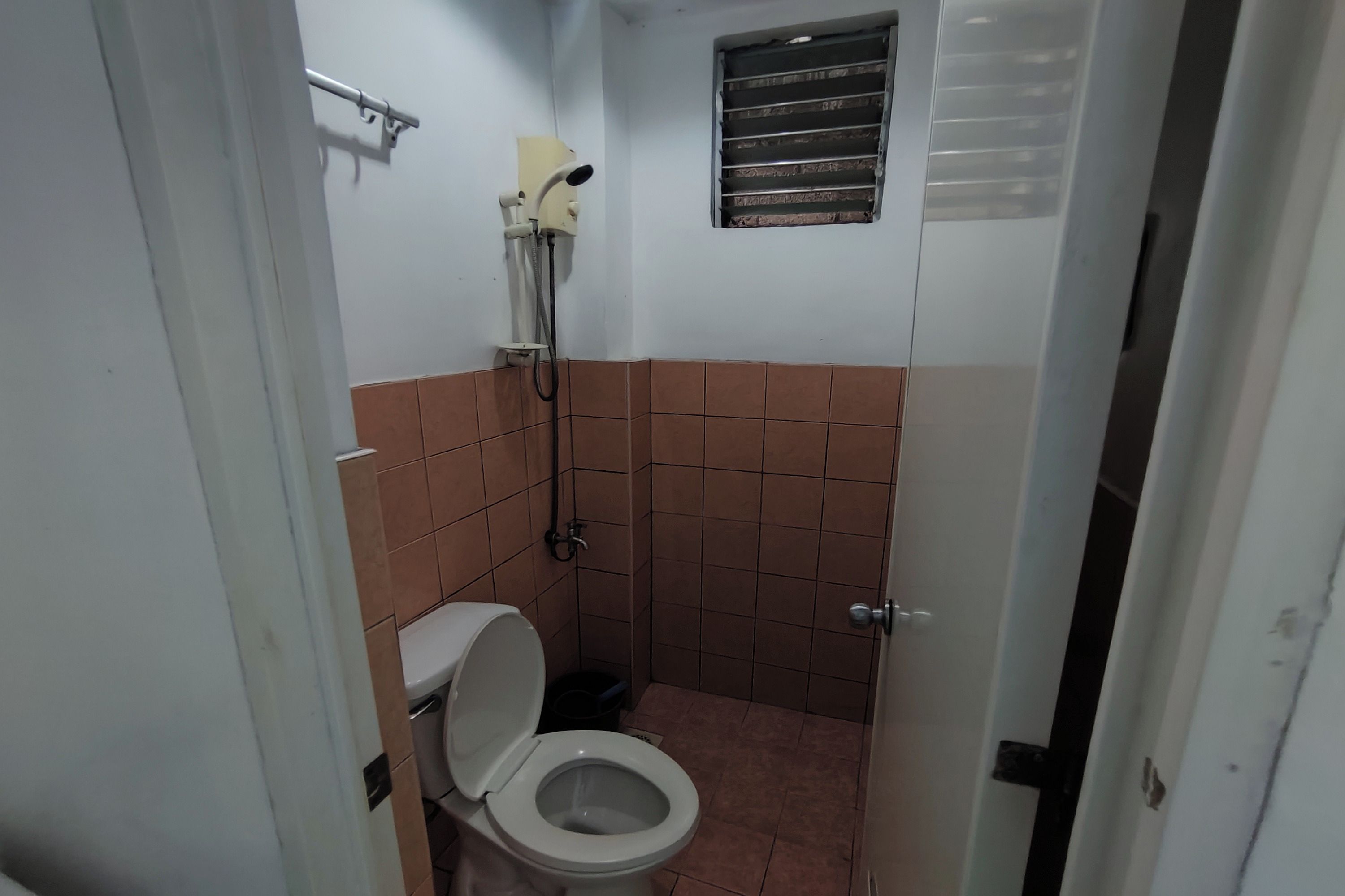 A small, compact bathroom with a toilet, shower, and a small window.