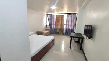 Una habitación de hotel con cama, un pequeño sofá, una mesa y un televisor montado en la pared.