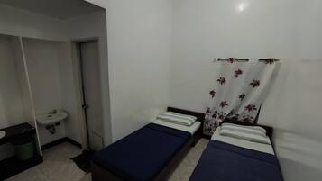Una habitación pequeña y limpia con dos camas individuales, un lavamanos y ducha.