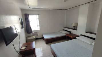 Una habitación de hotel con cama, escritorio, silla, televisor y ventana con cortinas.